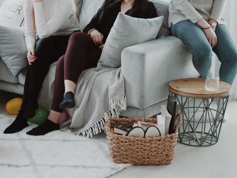 Kuvassa näkyy kolmen nuoren jalat, jotka istuvat sohvalla tai sohvan reunalla